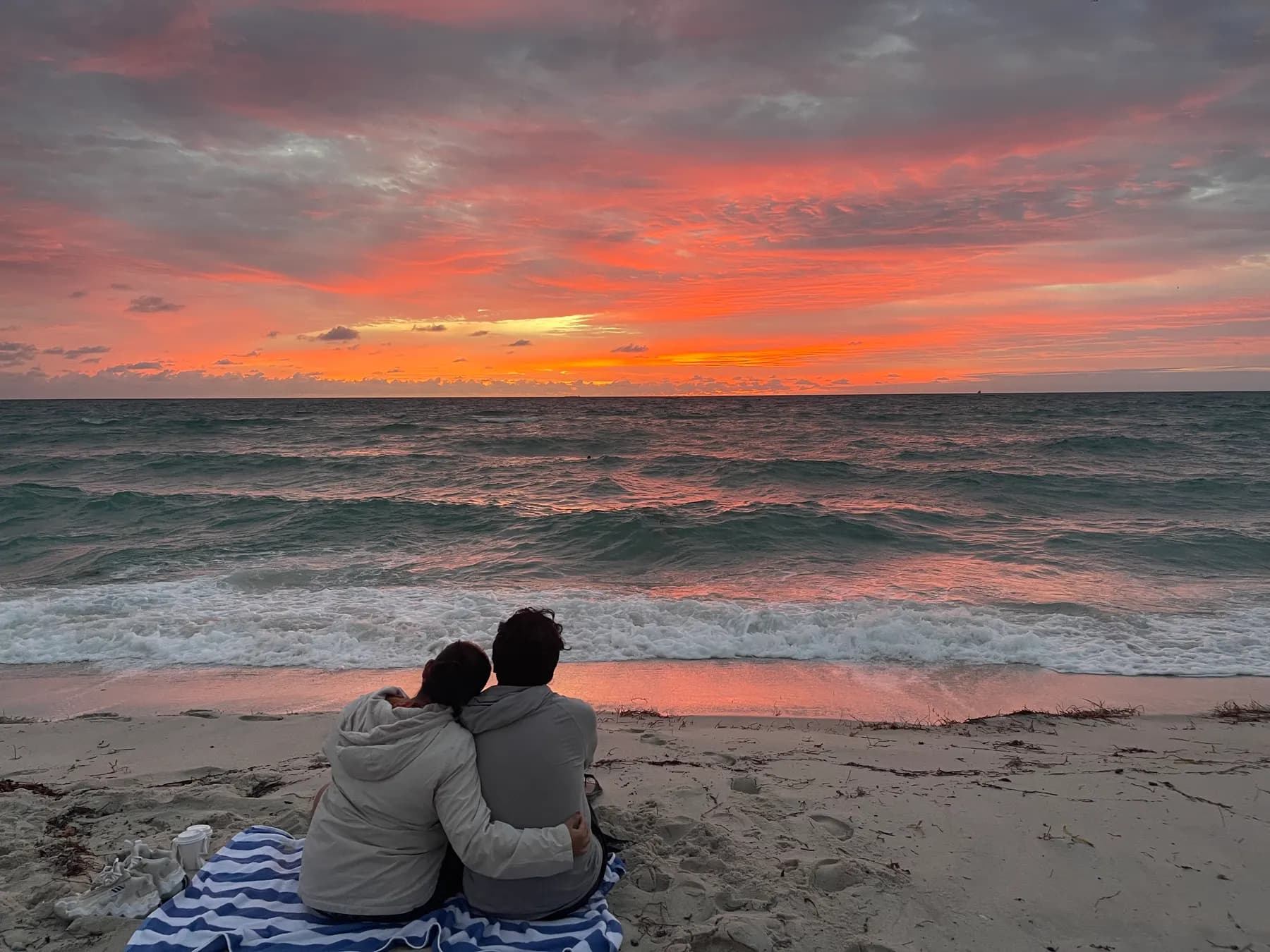 Couple sitting on a blanket on the sand under a pink and orange sunset
