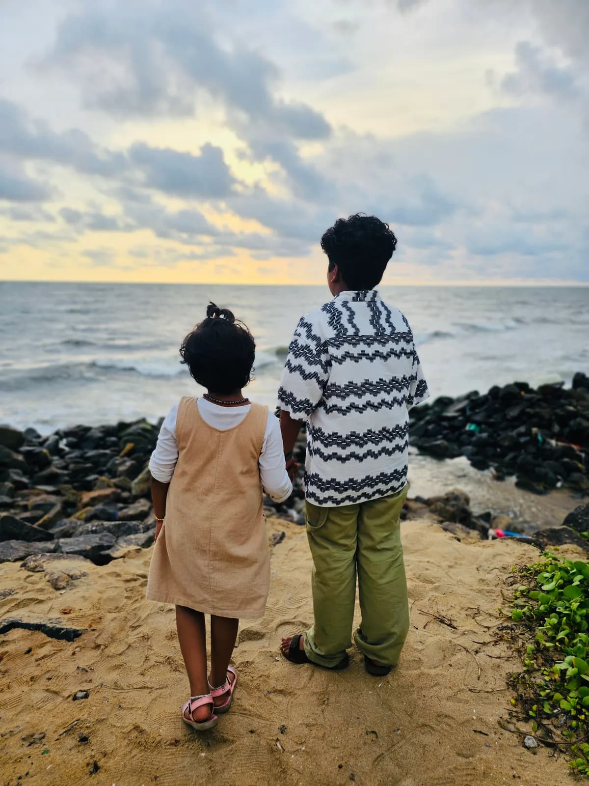 Two children standing at the edge of the water looking out to sea