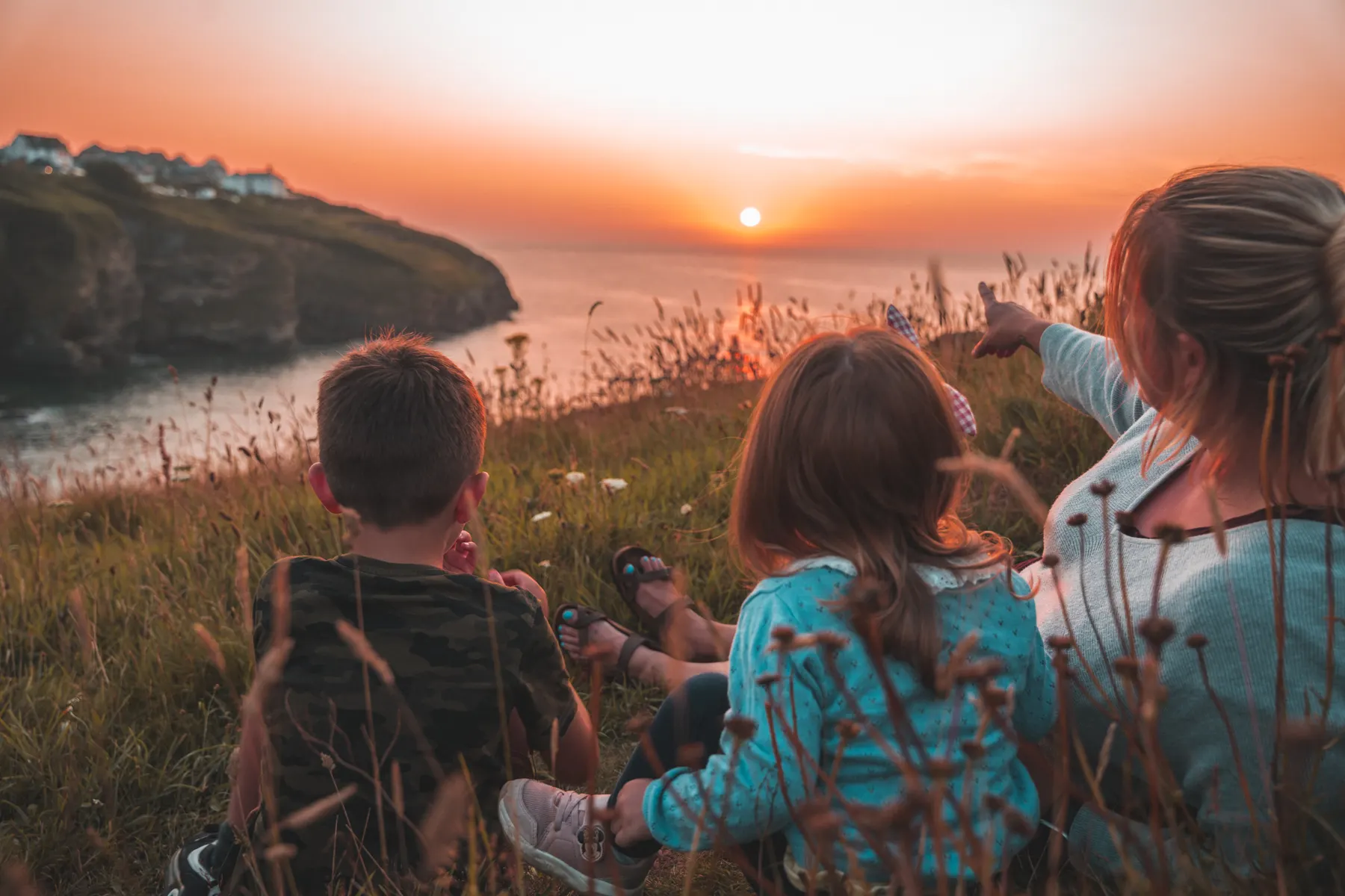 Family sitting together in tall grass watching the sun set over the water